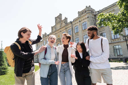 Cheerful student with backpack gesturing near multicultural friends outdoorsの写真素材