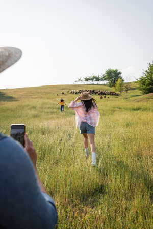 blurred man taking photo of wife and daughter running on green pasture in countrysideの写真素材