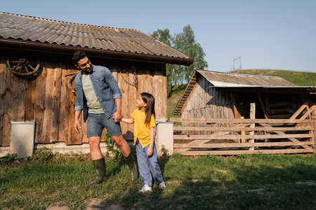 full length of father and daughter holding hands while walking on farm