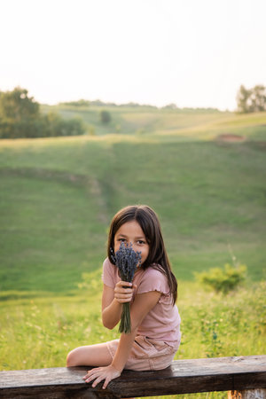 positive girl obscuring face with lavender bouquet and looking at camera in countrysideの写真素材
