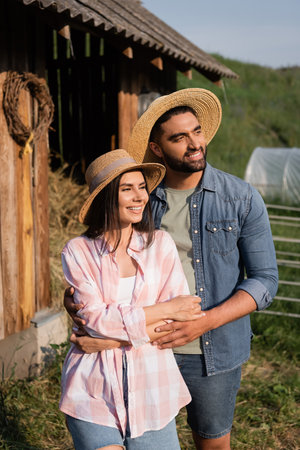 smiling couple in straw hats looking away on farm in countrysideの写真素材