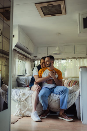 smiling gay man with tattoo hugging bearded boyfriend on bed in modern vanの写真素材