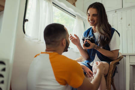 low angle view of happy gay man holding vintage camera and sitting in armchair near boyfriend in vanの写真素材