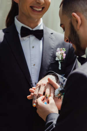 bearded gay man wearing wedding ring on finger of happy tattooed groomの写真素材