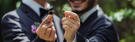 cropped view of happy and blurred gay men holding wedding rings in hands, bannerの写真素材