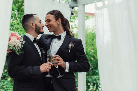 cheerful gay couple in suits toasting glasses of champagne on wedding dayの写真素材