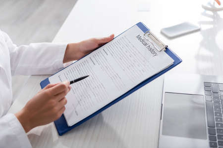 Cropped view of doctor holding medical history on clipboard near devices in clinic