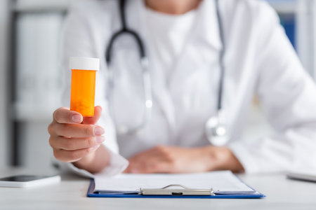 Cropped view of blurred doctor holding pills near clipboard and smartphone in clinicの写真素材
