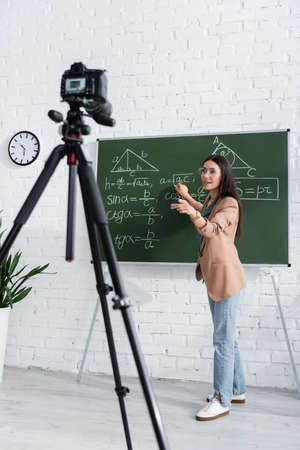 Teacher writing math formula on chalkboard near digital camera in classの写真素材