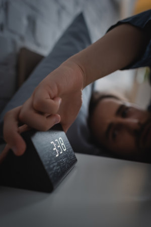 Blurred man taking electronic clock from bedside table at nightの写真素材