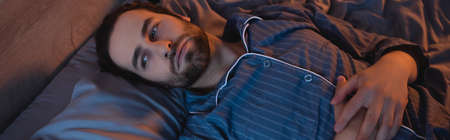 Young man suffering from insomnia on bed, banner