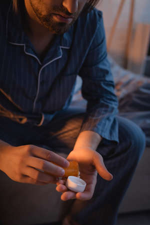 Cropped view of man with sleep disorder holding pills on bed at nightの写真素材