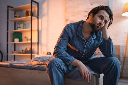 Tired man in pajama sitting on bed at nightの写真素材