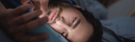 Young man suffering from sleepless and using smartphone in bedroom, banner