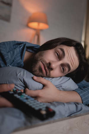 Man with insomnia holding blurred remote controller on bedの写真素材