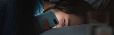 Man looking at smartphone on bed at night, bannerの写真素材