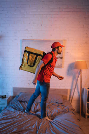 Side view of sleepwalker in uniform with thermo backpack standing on bed at nightの写真素材