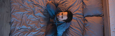 Overhead view of man with closed eyes sitting on bed at home, banner