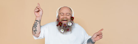 happy overweight man with flowers in beard listening music in headphones isolated on beige, bannerの写真素材
