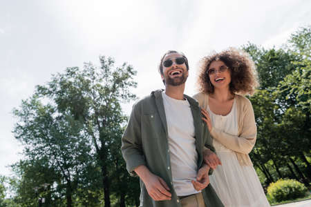 joyful man and happy curly woman in trendy sunglasses smiling in parkの写真素材