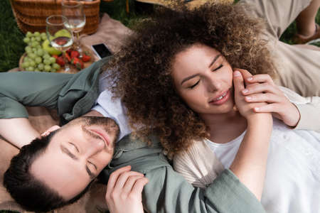 top view of curly woman lying on pleased boyfriend during picnic in summer parkの写真素材