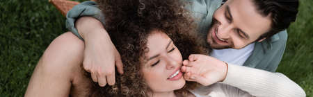 top view of curly woman lying on happy boyfriend during picnic in summer park, banner