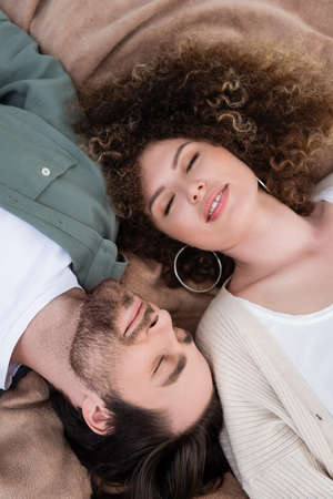top view of happy young woman and man with closed eyes lying on soft blanketの写真素材