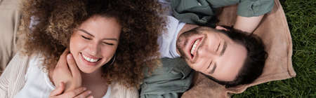 top view of cheerful woman lying on happy boyfriend during picnic in summer park, banner
