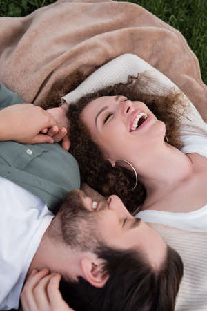 top view of joyful young woman and man with closed eyes laughing while lying on soft blanket