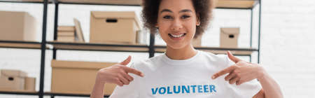 happy african american woman pointing at volunteer lettering on t-shirt, banner