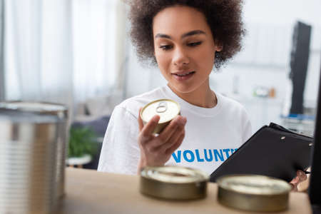 smiling african american woman with clipboard holding canned food in charity centerの写真素材