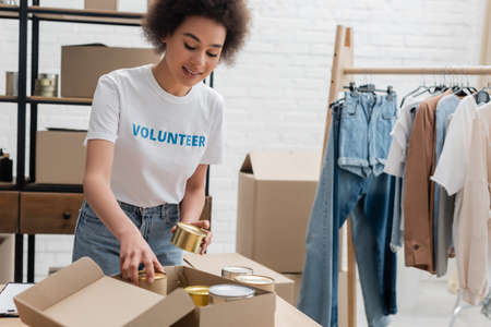 african american volunteer packing canned foodstuff in charity centerの写真素材