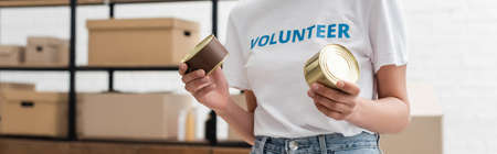 partial view of african american volunteer holding canned food in charity warehouse, banner