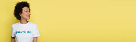 african american volunteer smiling while looking away isolated on yellow, bannerの写真素材