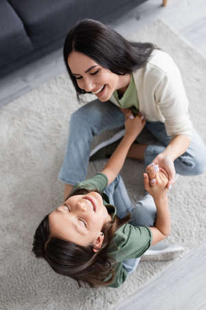 top view of cheerful babysitter and girl having fun on carpet at homeの写真素材