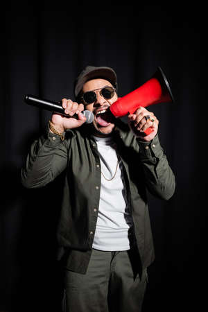 emotional indian hip hop performer in sunglasses and cap screaming in microphone and loudspeaker on...