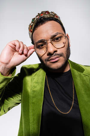 eastern hip hop performer in green velvet blazer and crown adjusting isolated on grey