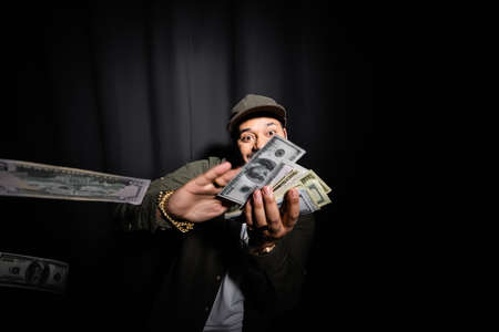 rich indian hip hop performer throwing dollar banknotes on blackの写真素材
