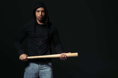 African american man in hoodie holding baseball bat and looking at camera isolated on blackの写真素材