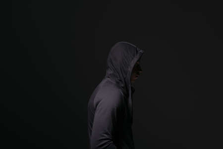 Side view of african american hooligan in hood standing isolated on blackの写真素材