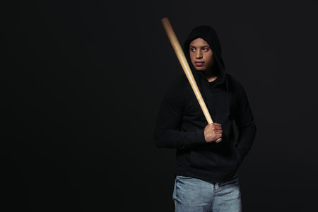 African american hooligan with baseball bat looking away isolated on blackの写真素材