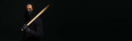 African american hooligan with mask on face holding baseball bat isolated on black, bannerの写真素材