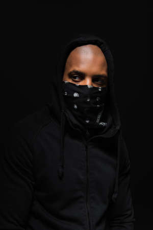 African american bandit with scarf on face looking away isolated on blackの写真素材