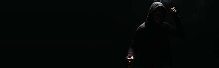 Silhouette of african american bandit in hoodie and gloves holding knife isolated on black, banner