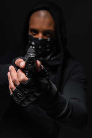 Blurred african american bandit with mask on face holding gun isolated on blackの写真素材