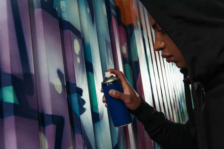 Side view of african american hooligan in hoodie drawing graffiti on wall on urban streetの写真素材