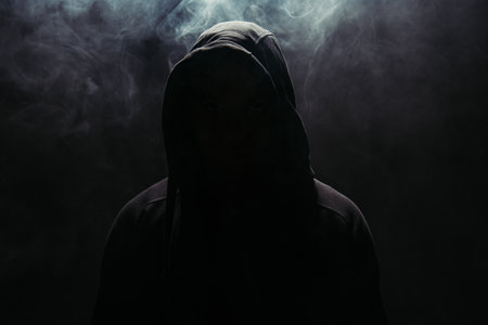 Silhouette of hooligan in hood on black background with smokeの写真素材