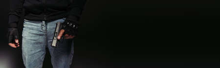 Cropped view of african american bandit in gloves holding gun on black background, banner