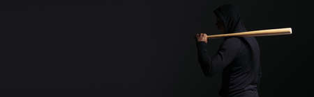 Side view of african american man in hoodie holding baseball bat isolated on black, bannerの写真素材