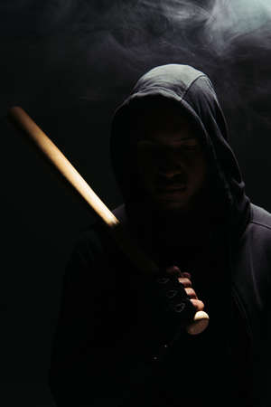 Silhouette of african american bandit in hood and glove holding baseball bat on black background with lighting and smokeの写真素材